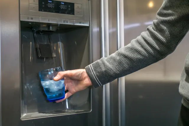 Hand filling a glass with ice and water at the door dispenser of a refrigerator ice maker leaking water