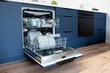 Open dishwasher with racks of plates and cups pulled out in a blue kitchen