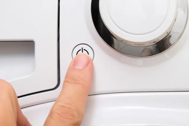 Finger pressing the power button on the control panel of a washing machine that won't start