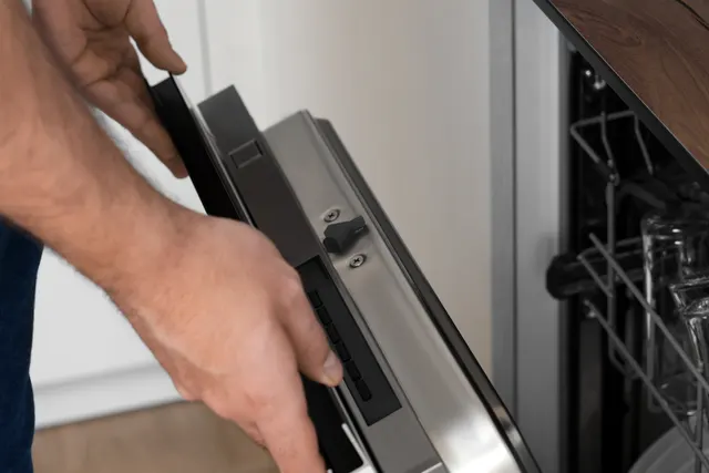 Person holding a dishwasher door near the latch and top controls