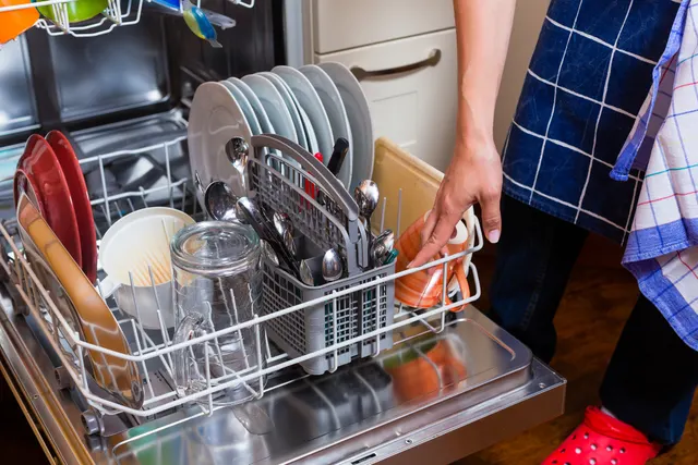 Person pulling out a loaded dishwasher rack with plates, glasses, and utensils
