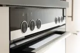 Close-up of a stainless steel range control panel with round black knobs above the oven door