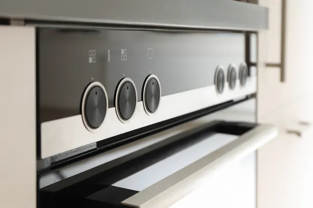 Close-up of a stainless steel range control panel with round black knobs above the oven door